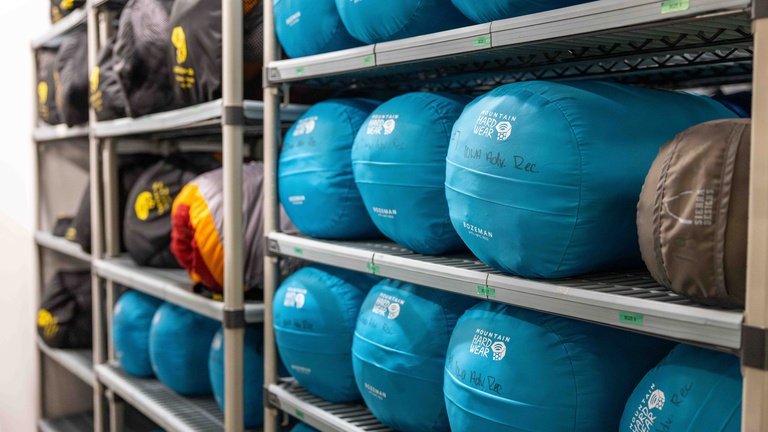 A photo of sleeping bags stacked together on a shelf horizontally.