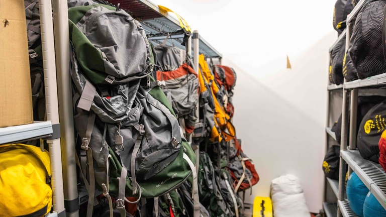 A photo of empty hiking or backpacking backpacks. They are hanging on different hangers and are there are multiple different colors of bags.