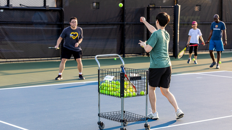 Adult participants taking an adult tennis lesson on the outdoor courts at the Hawkeye Tennis and Recreation Complex.