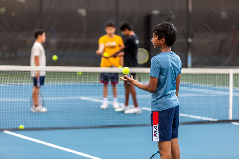 Junior tennis player on the outdoor tennis courts. He is holding a tennis racket and tossing a tennis ball up. 