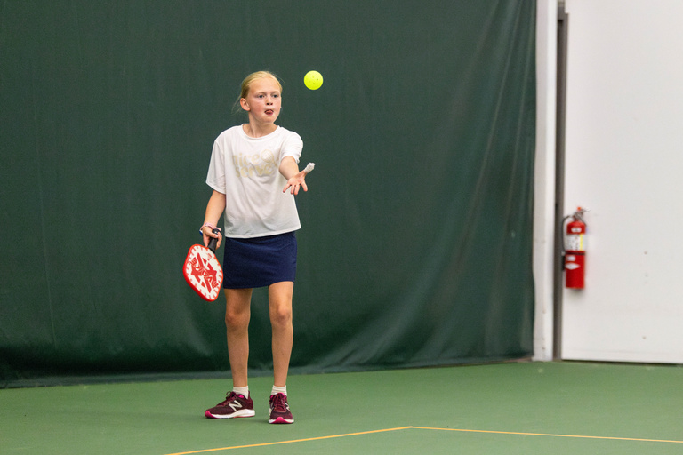 Junior player holding a pickleball paddle and tossing a waffle ball in the air.