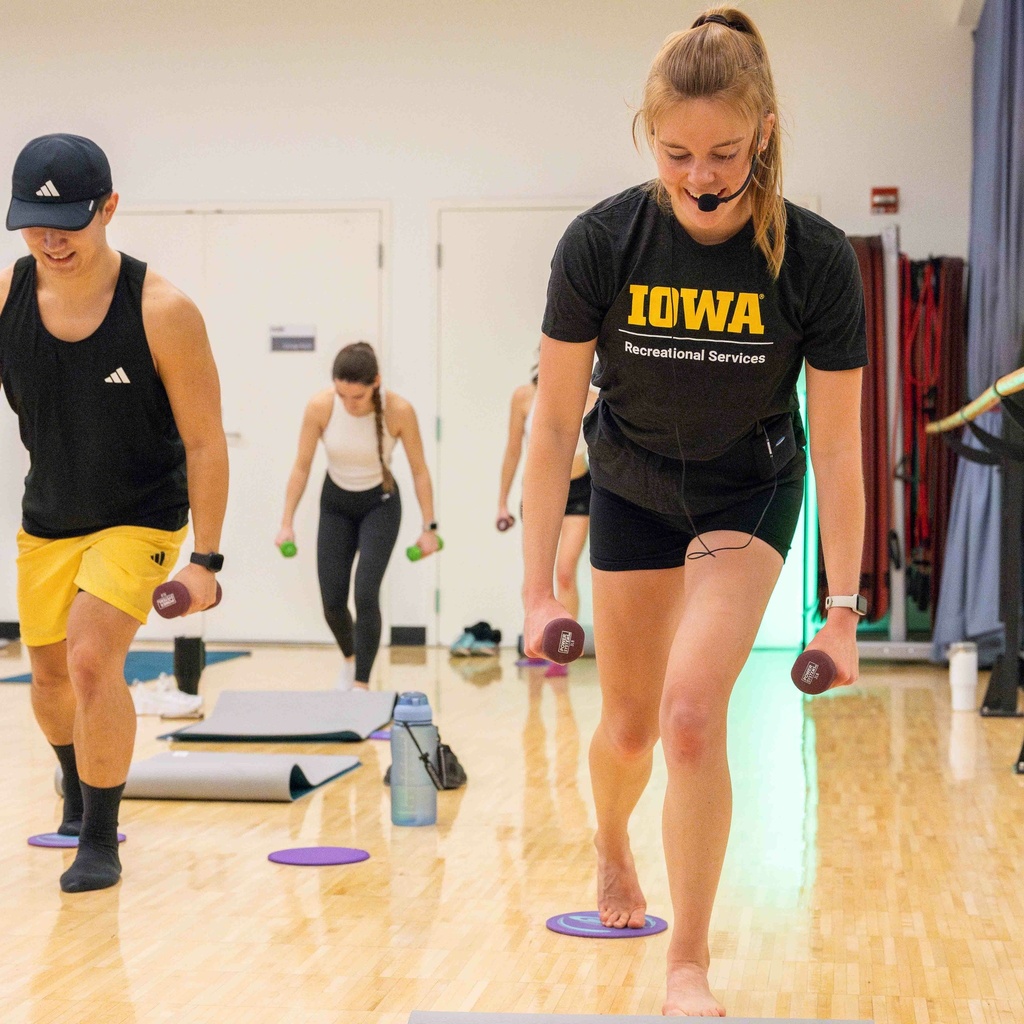 Group fitness participants taking part in a class. The group is facing the camera and standing with small dumbbells in their hands.