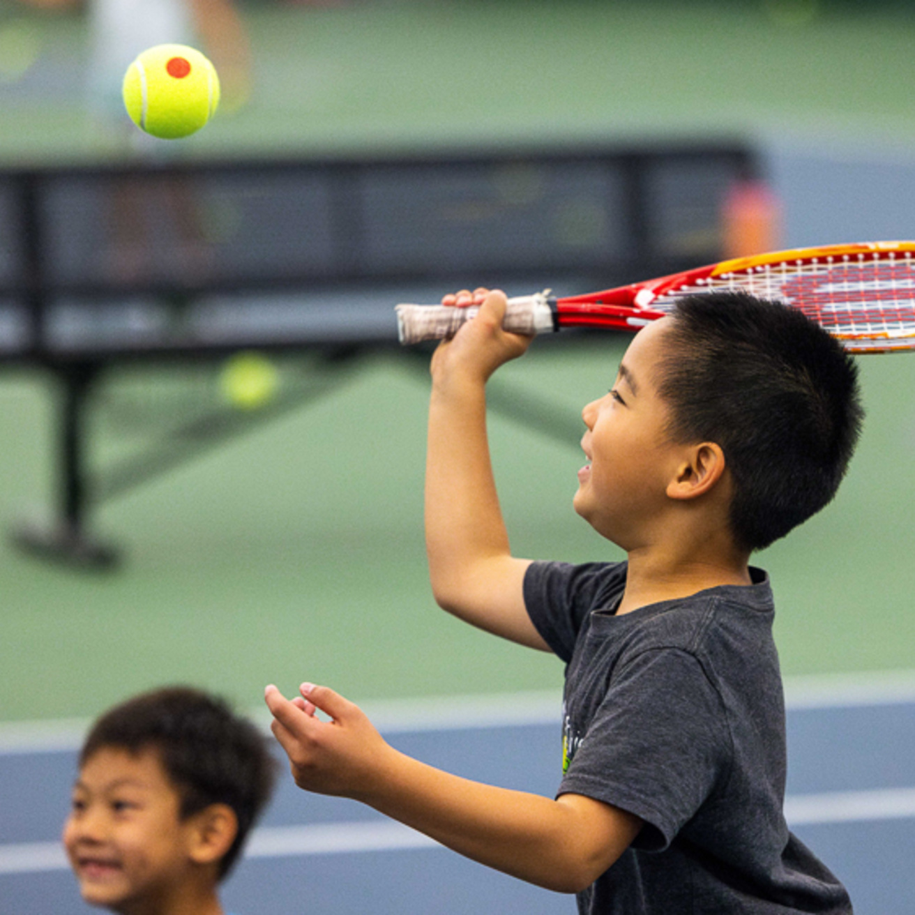 A junior participant swinging a racquet at a ball while playing tennis on the indoor courts at the Hawkeye Tennis and Recreation Complex.
