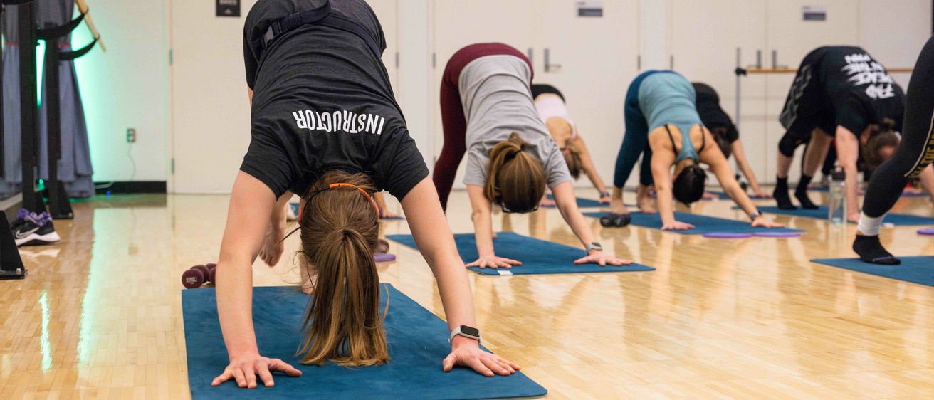Group fitness instructor modeling a yoga position as the rest of the class follows along.