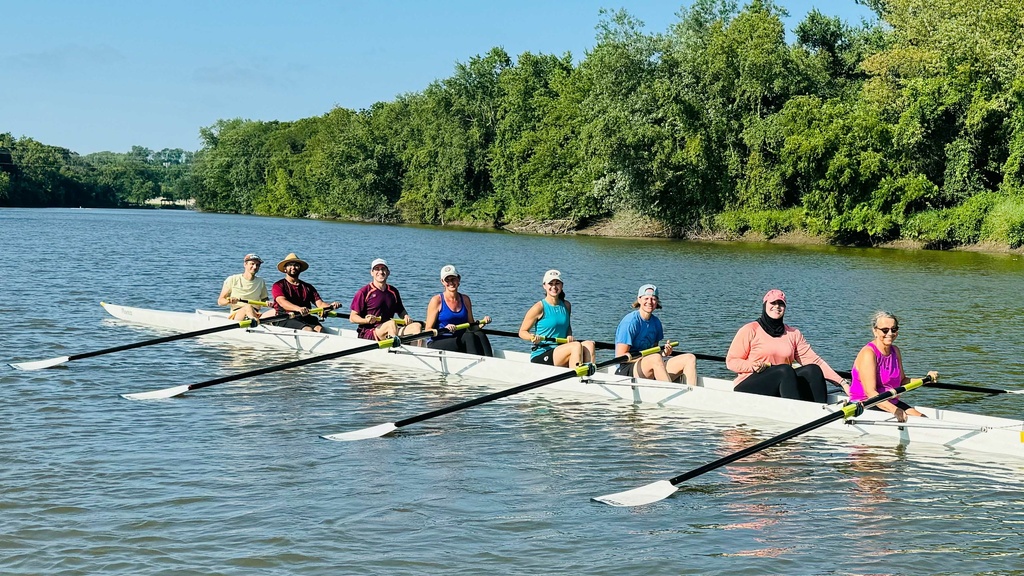 A boat and crew posing for a photo on the Iowa River. People participating in a Learn to Row class.