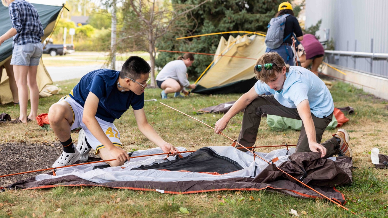 Two male students setting up a tent outside the Outdoor Rental Center.