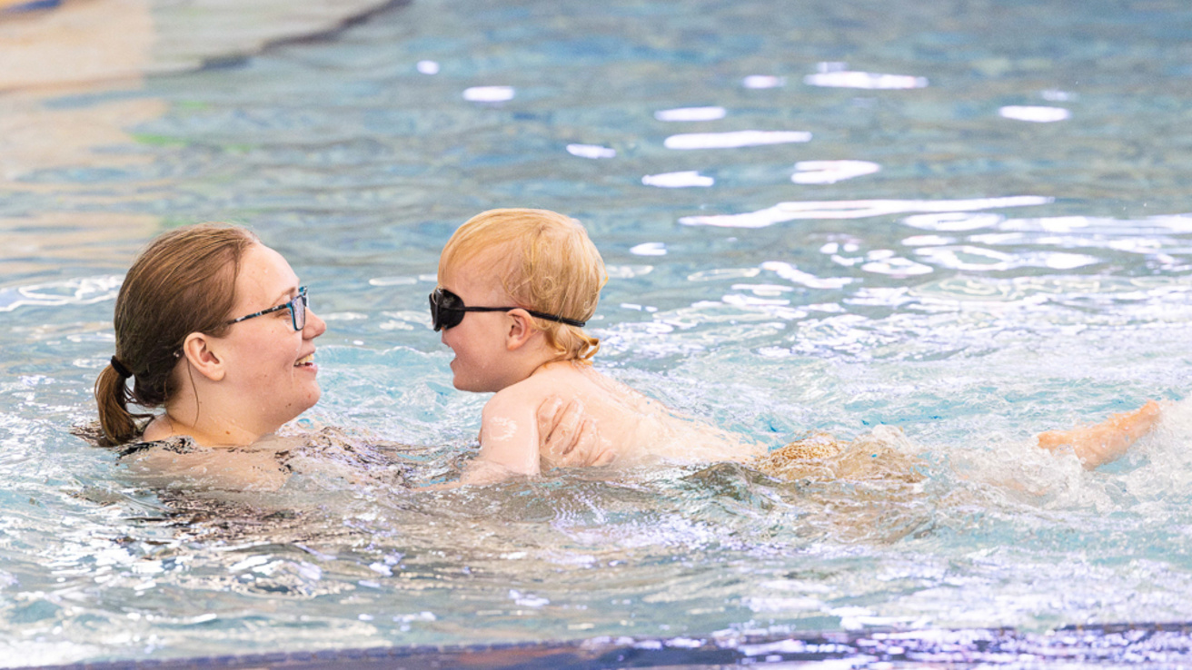 An adult swim lesson instructor in the pool with a child, teaching them how to swim.